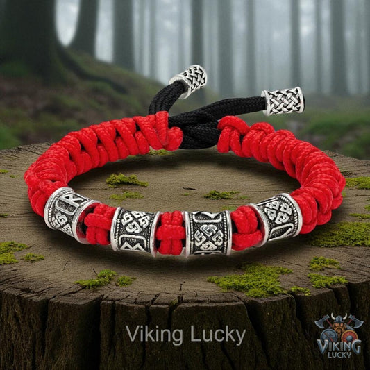 Red and black braided bracelet with silver Viking-style beads on a wooden stump with a forest background.