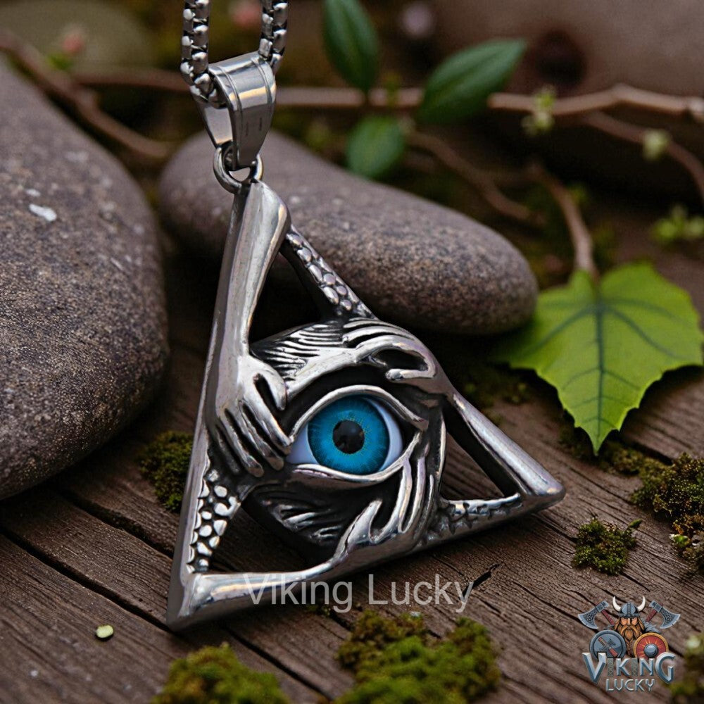 Silver eye-shaped pendant with blue gemstone on a wooden surface with leaves and stones.