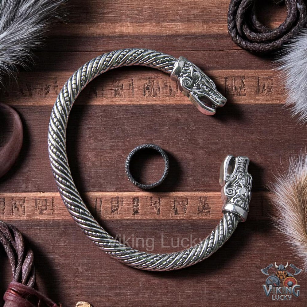 Intricate silver Viking armring with detailed dragon serpent heads on a dark wood background with runes and fur.