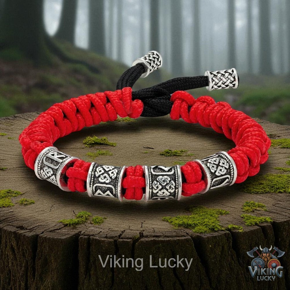 Red and black braided bracelet with silver Viking-style beads on a wooden stump with a forest background.