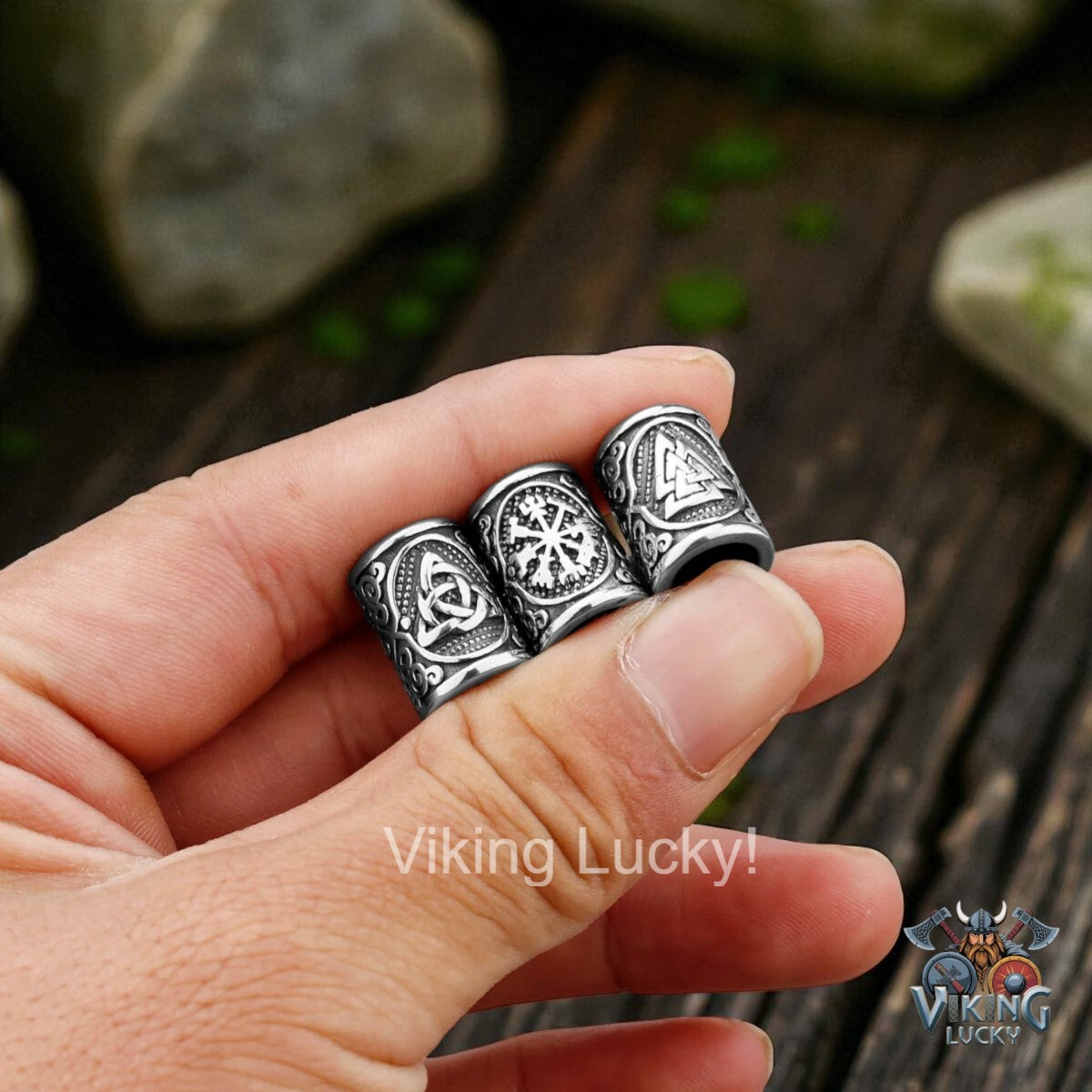 Three silver rings with intricate designs held between fingers against a wooden background.