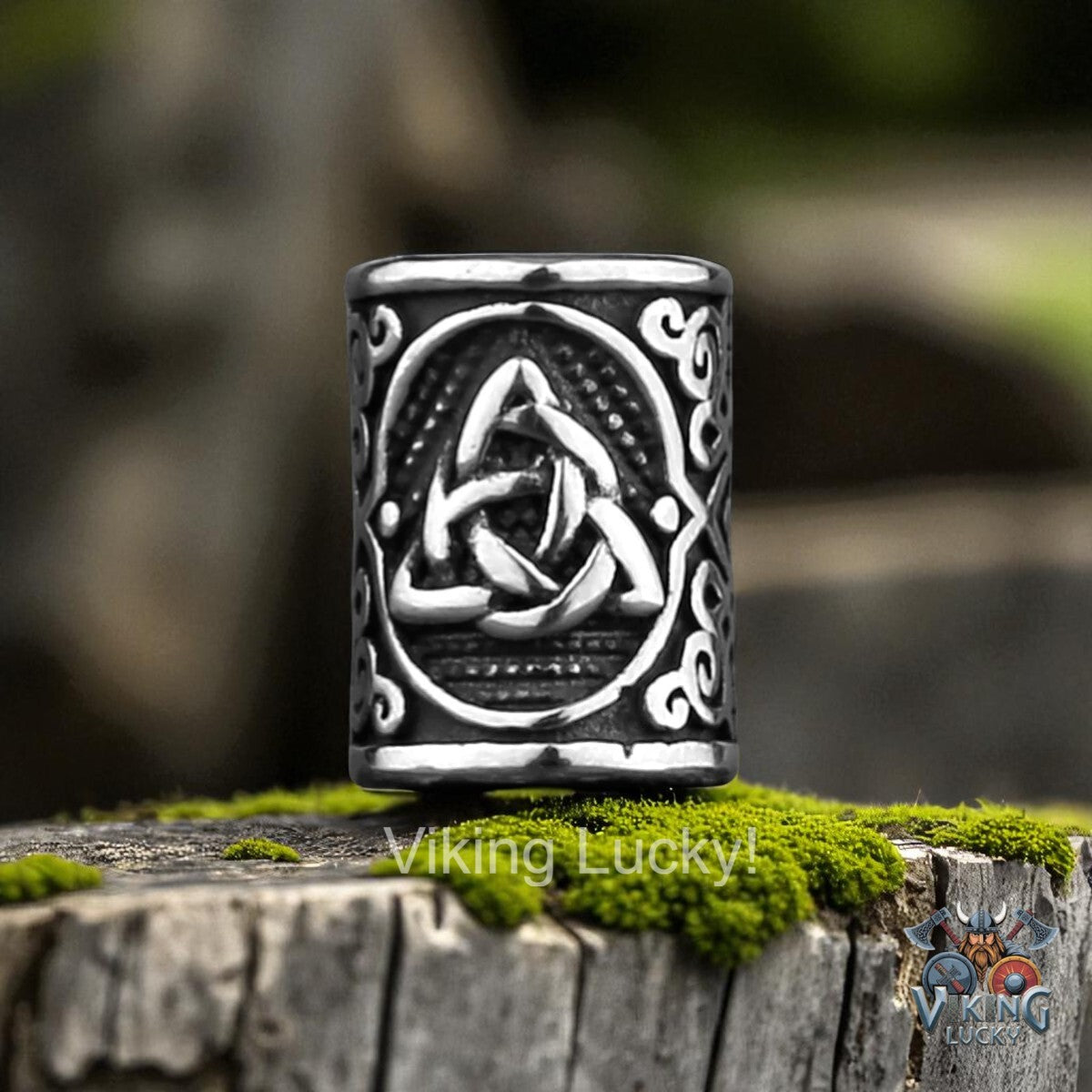 Black and silver ring with Celtic knot design on a stone surface with grass