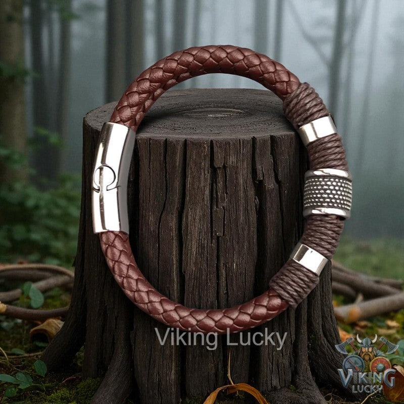 Brown braided leather bracelet with silver accents on a wooden stump in a forest setting, featuring 'Viking Lucky' branding.