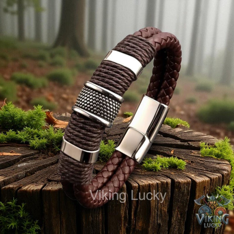 Brown braided bracelet with silver accents on a wooden log in a forest setting, featuring 'Viking Lucky' branding.