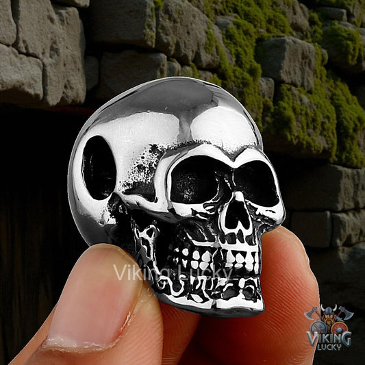 Silver skull-shaped pendant held by a hand against a stone wall background