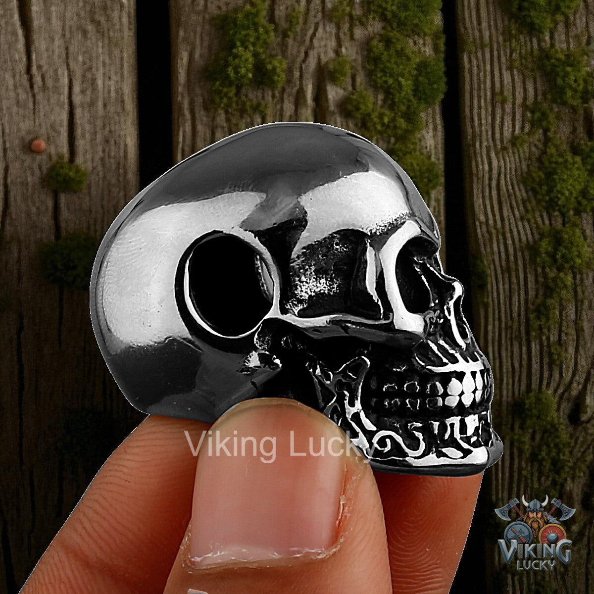 Silver skull-shaped object held between fingers with a wooden background VikingLucky