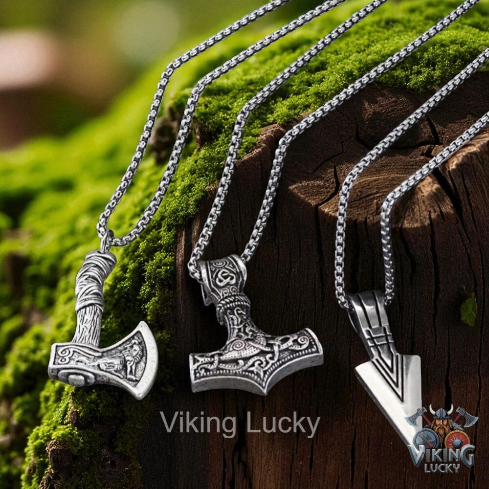 Three silver Viking-themed necklaces on a wooden surface with moss